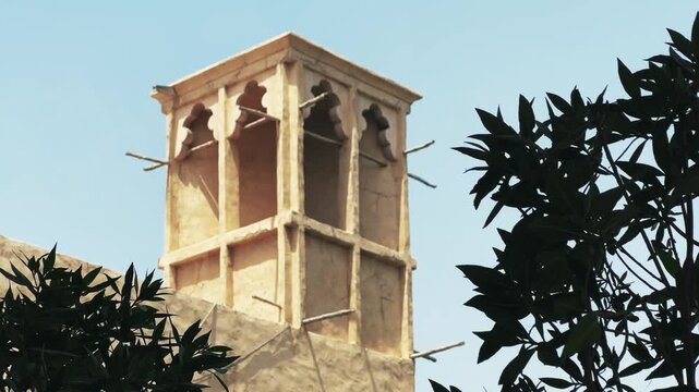 Wind tower house detail characteristic of traditional Arabian architecture, set against a clear sky and framed by lush greenery