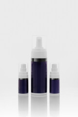 Set of three airless cosmetic pump bottles in different sizes on white reflective background—blank packaging mockup for skincare branding and product lineup.