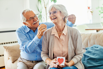 Smiling senior woman receives a luxury present a necklace and present box from  her husband at home