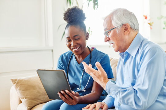 Doctor or nurse caregiver showing a tablet screen to  senior man and laughing at home or nursing home