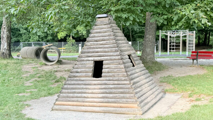 Obraz premium Wooden pyramid hut in playground, outdoor eco playhouse for children, rustic wooden structure for kids fun and recreation, natural park equipment for family leisure activities. High quality photo