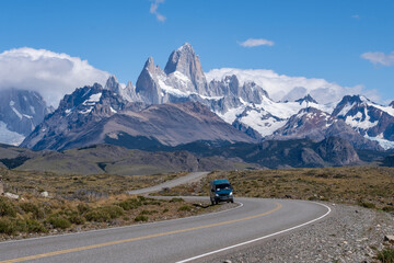 Fototapeta premium Scenic road trip in Patagonia with a van driving towards the iconic Mount Fitz Roy, surrounded by dramatic peaks, glaciers, and clear blue skies