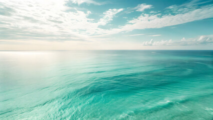 Obraz premium A vast expanse of turquoise ocean water under a cloudy sky, with gentle waves and sunlight reflecting on the surface.