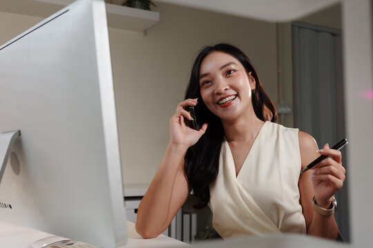 Cheerful asian businesswoman talking on phone and taking notes in office - Powered by Adobe