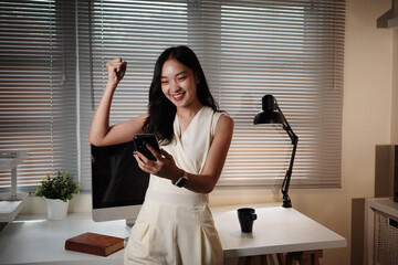 Excited businesswoman celebrating success while holding smartphone in home office