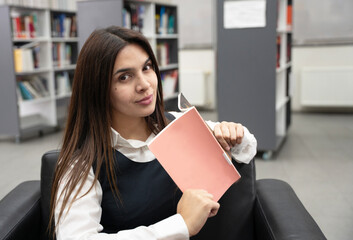 Woman reading a book, peeking over its cover, library setting