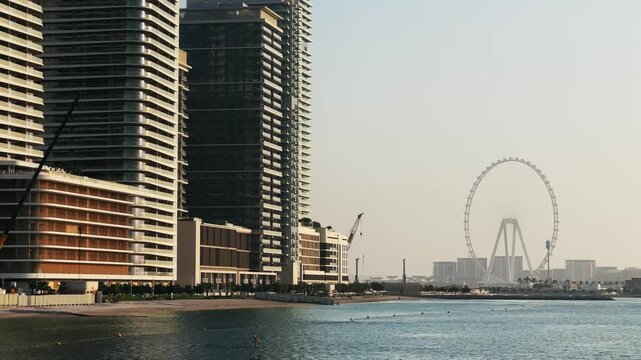 Dubai skyline by the waterfront showing skyscraper cityscapes landmarks and Ferris Wheel at sunset, no logos