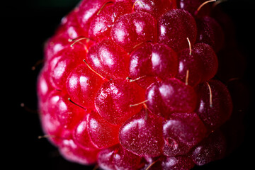 Close-up shot of a raspberry showing the details of the red fruit's texture. Black background.