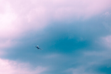 Passenger airplane flying high above the clouds on a sunny day with a blue and purple sky, symbolizing international travel, freedom, and adventure