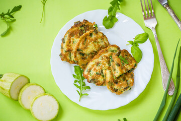 fried zucchini pancakes with green onions in a plate on a green background