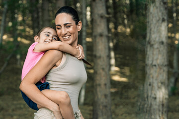 Fototapeta premium Happy mother and daughter hugging during a piggyback ride in the forest, with copy space.