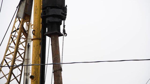 Close-up view of pile driver picking up concrete pile at a construction site before hammering. Overcast sky. Real time video. Deep foundation theme.