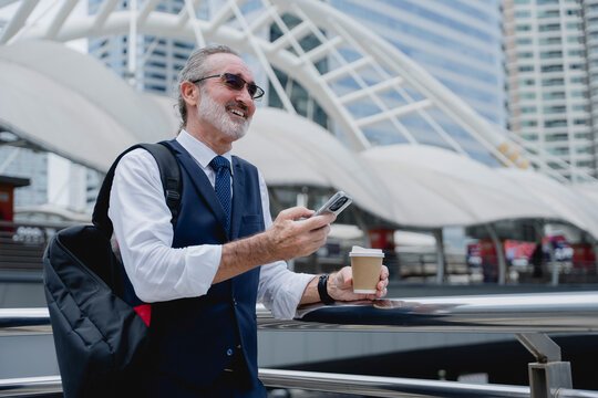 Confident senior businessman in suit holding coffee and using smartphone for video call in modern city, symbolizing leadership, communication, technology, and professional lifestyle.