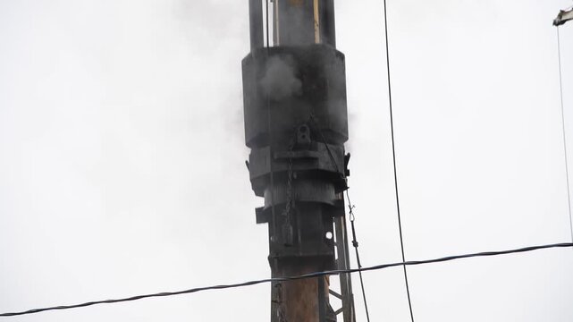 Close-up view of pile driver hammering concrete pile at a construction site. Overcast sky. Real time video. Deep foundation theme.