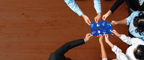 A diverse team gathers around a blue board, collaborating on a strategy session. The wooden surface enhances the focus on teamwork and creative planning for business success. Amity