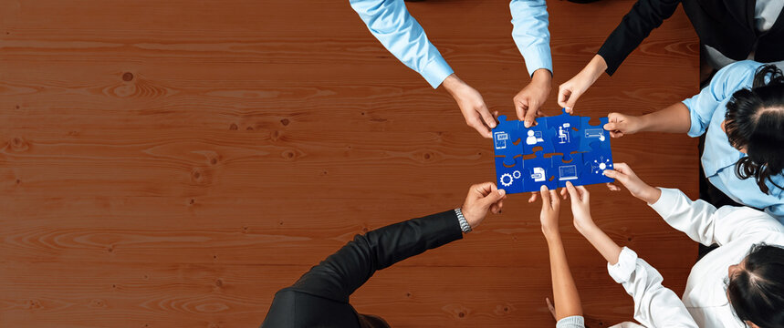A diverse team gathers around a blue board, collaborating on a strategy session. The wooden surface enhances the focus on teamwork and creative planning for business success. Amity