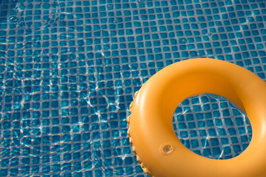 Bright yellow float ring rests on the surface of a sparkling blue swimming pool during a sunny afternoon in summer
