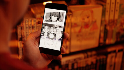 Reading anime maid girls digital manga comic on smartphone beside a shelf with books over shoulder view