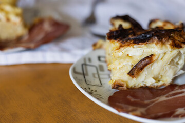 Delicious slice of homemade potato casserole served on a stylish plate with sliced meat in a cozy kitchen setting