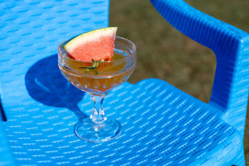 Refreshing cocktail with watermelon garnish sits on a vibrant blue chair in a sunny outdoor setting...