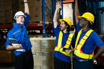 Three multicultural warehouse workers, Caucasian male adult, Hispanic male adult, and African male adult, celebrating teamwork success raising hands with happy smiles inside warehouse facility