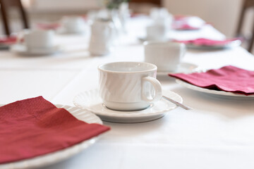 Empty coffee cups and plates with red napkins on a large table. Objects related to tea time and eating cake with the family. Decoration at a birthday party in a restaurant.