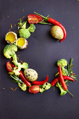Creative letter G formed with chili peppers, broccoli, rosemary, quail eggs, tomatoes and olive oil on dark background. Unique food typography for culinary, healthy lifestyle or design projects