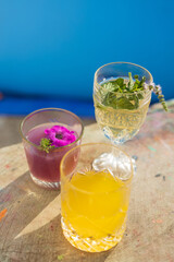 Refreshing summer beverages with colorful garnishes served on a sunny terrace overlooking a vibrant blue background