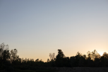 Beautiful sunset casts warm glow over peaceful landscape with silhouettes of trees in the background