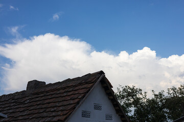 Beautiful clouds drift over a rustic house under a clear blue sky in the afternoon sun with greenery in the foreground