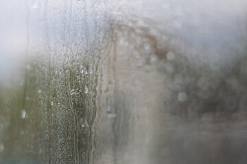 Rain droplets create a misty effect on a fogged window in a cozy indoor space during a rainy day