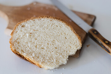 Freshly sliced white bread rests on a wooden cutting board beside a sharp knife in a kitchen setting during the morning hours