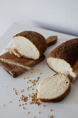 Freshly baked artisanal bread on a wooden cutting board with wheat grains scattered nearby in a minimalist kitchen setting
