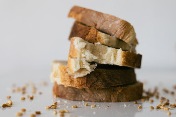 Slices of fresh bread stacked on a white surface with scattered seeds around them in a bright kitchen setting