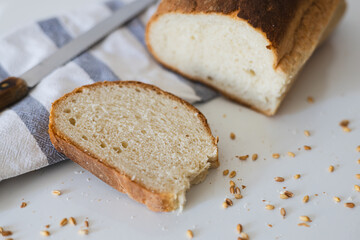 Freshly baked loaf of bread with a slice cut, lying on a striped cloth with scattered grains on a kitchen counter
