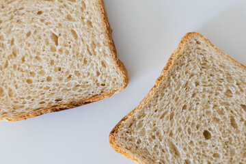 Two slices of toasted whole grain bread on a plain white surface in a bright kitchen setting during the morning hours, perfect for breakfast preparation or sandwich making