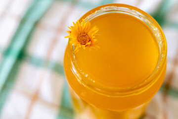 Homemade golden herbal drink topped with bright flower on a checkered cloth in a cozy kitchen...