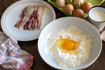 Breakfast preparation with fresh eggs, flour, and bacon on a wooden table during the morning hours