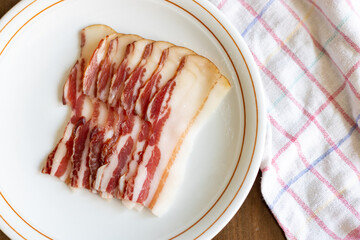 Slices of cured meat arranged neatly on a white plate with a checkered towel beside it during a casual dining setting