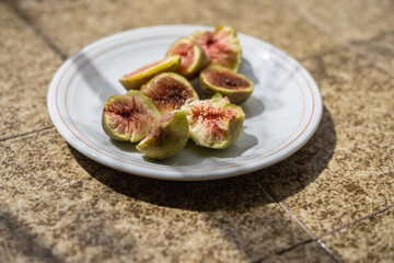 Freshly sliced figs on a white plate resting under warm sunlight on a textured surface in the afternoon