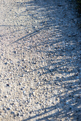 Evening shadows cast on a gravel path highlight the undulating surface of a serene outdoor environment in a countryside setting
