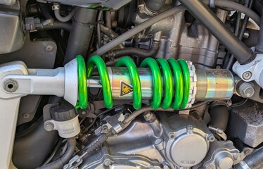 Vista de cerca del amortiguador de la suspensi&oacute;n de una moto, con el motor de fondo 