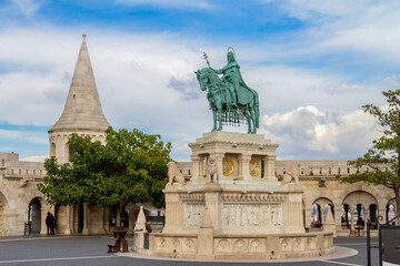 Obraz premium Impressive bronze equestrian statue of King Saint Stephen against Fisherman's Bastion arches and towers under sunny blue sky. Budapest, Hungary.