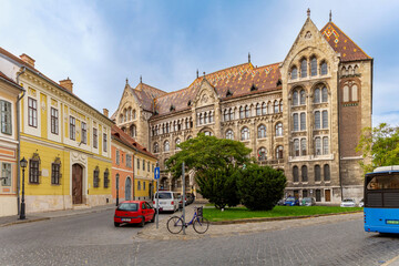 Fototapeta premium Vienna Gate Square dominated by Neo-Gothic National Archives with Zsolnay tiles, surrounded by Old Buda's pastel houses under hazy blue sky. Budapest, Hungary.