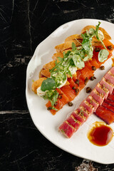 Elegant seafood platter with assorted fish delicacies. Slices of smoked salmon with toasted bread, fresh greens, and cream sauce, alongside seared tuna and marinated fish served with soy sauce. Gourme
