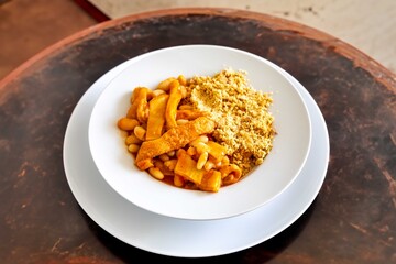 A classic Brazilian dish known as dobradinha, prepared with beef tripe, white beans, and tropical spices, served with traditional farofa made from toasted cassava flour.