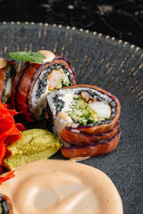 Close-up of sushi rolls combining salmon, mango, cucumber, and cream cheese inside rice and nori. Topped with thin salmon slices 