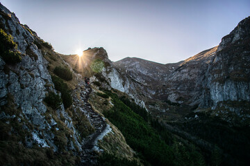 Obraz premium the sun breaking through the mountain peaks on the mountain trail