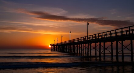 Fototapeta premium Stunning sunrise paints sky vibrant orange over tranquil ocean pier with gentle waves