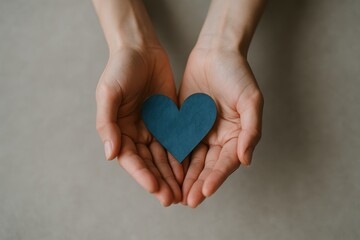 Fototapeta premium Elegant woman holding delicate blue paper heart symbol with gentle hands against soft neutral background representing compassion